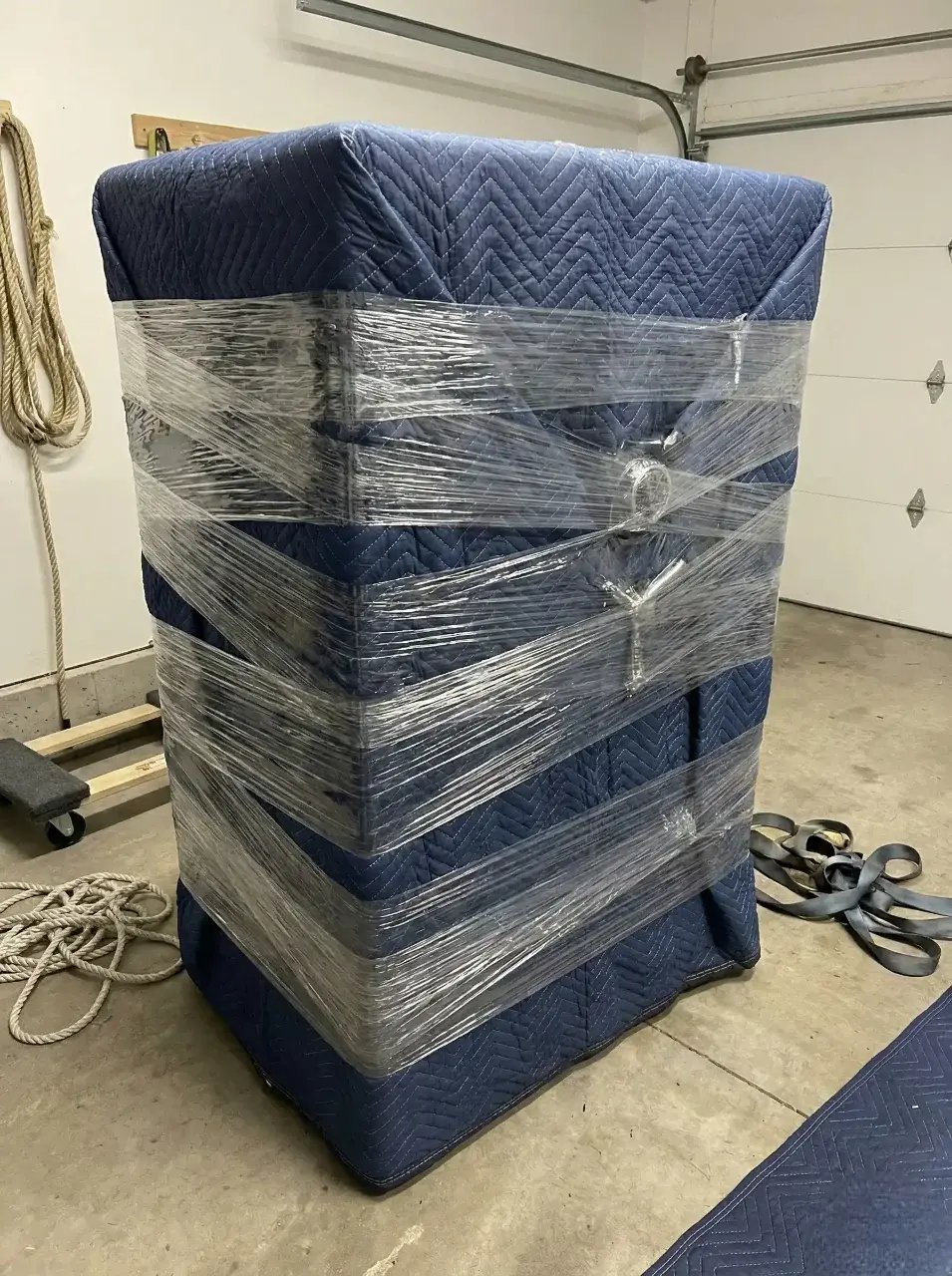 Gros meuble entièrement emballé dans des couvertures de déménagement bleues et du film plastique protecteur. Gros meuble entièrement emballé dans des couvertures de déménagement bleues et du film plastique protecteur.