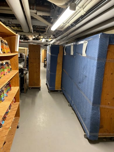Rayonnages de bibliothèque emballés dans des couvertures de déménagement, sur plateformes roulantes, dans un corridor de sous-sol