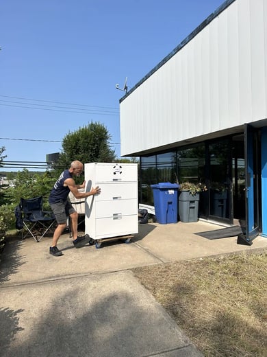 Déménageur roulant un classeur sur un diable devant un immeuble commercial, lors d'un déménagement de bureaux