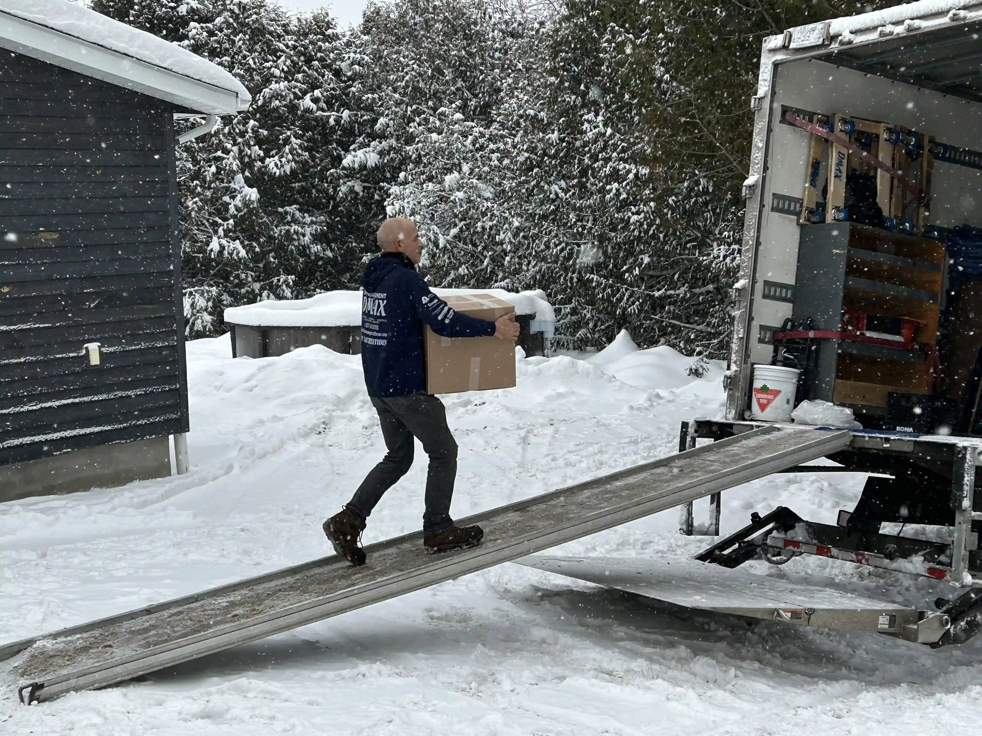 Déménageur DMAX transportant une boîte en carton sur une rampe de camion pendant un déménagement hivernal à Joliette, avec neige abondante Déménageur DMAX transportant une boîte en carton sur une rampe de camion pendant un déménagement hivernal à Joliette, avec neige abondante