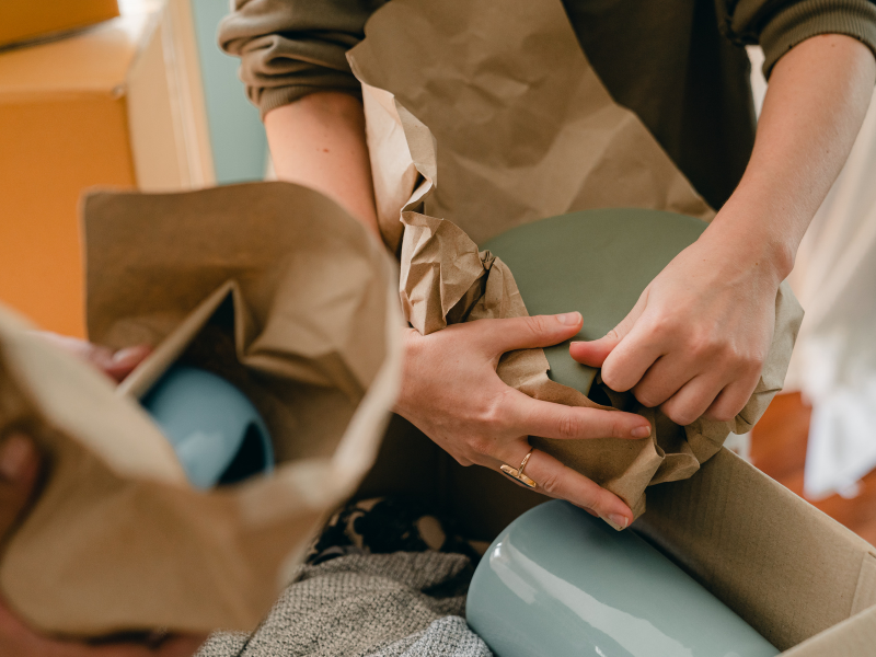 Packing fragile dishware with protective paper for a move, showing hands carefully wrapping items for transport.
