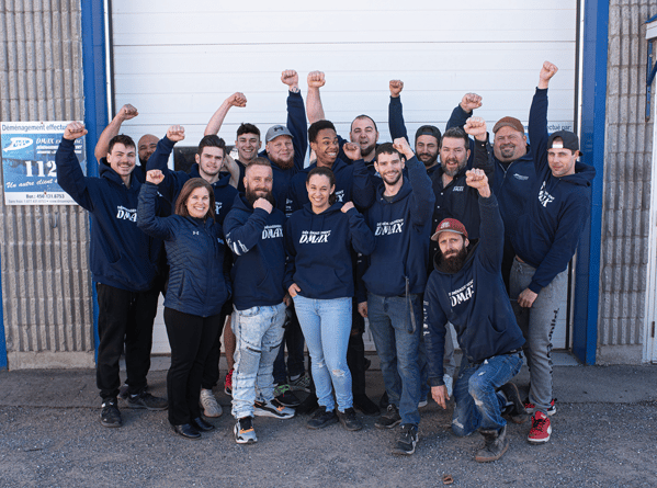 Best Mover Montreal: DMAX moving team posing together in front of a warehouse, raising their arms as a sign of determination and team spirit.