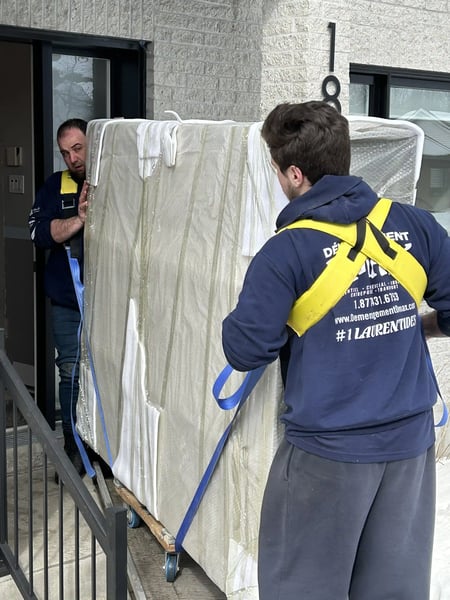 Best Montreal Mover: Two DMAX movers transporting a large, protected piece of furniture during a residential move, using safety straps.