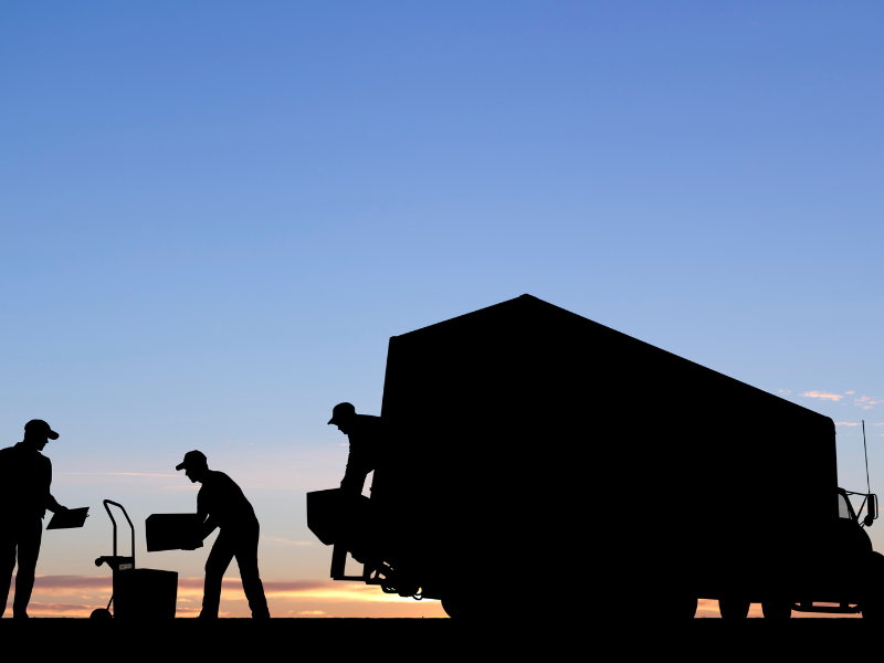 Silhouettes of movers loading items into a truck at sunset.