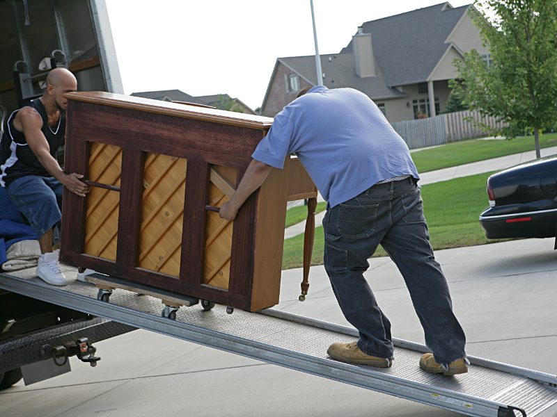 Two movers transporting a piano into a truck using a ramp.