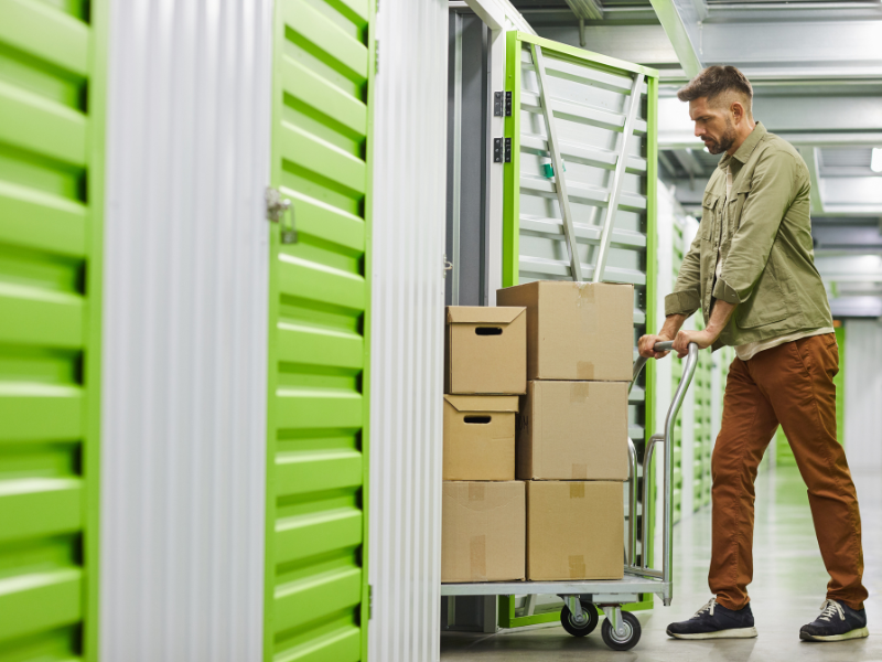 Man using a dolly to move boxes into a storage unit.