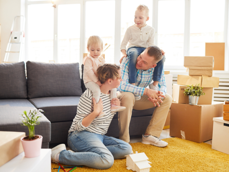 un couple avec un enfant chacun sur les épaules assis dans un salon - Comment bien préparer son déménagement ?