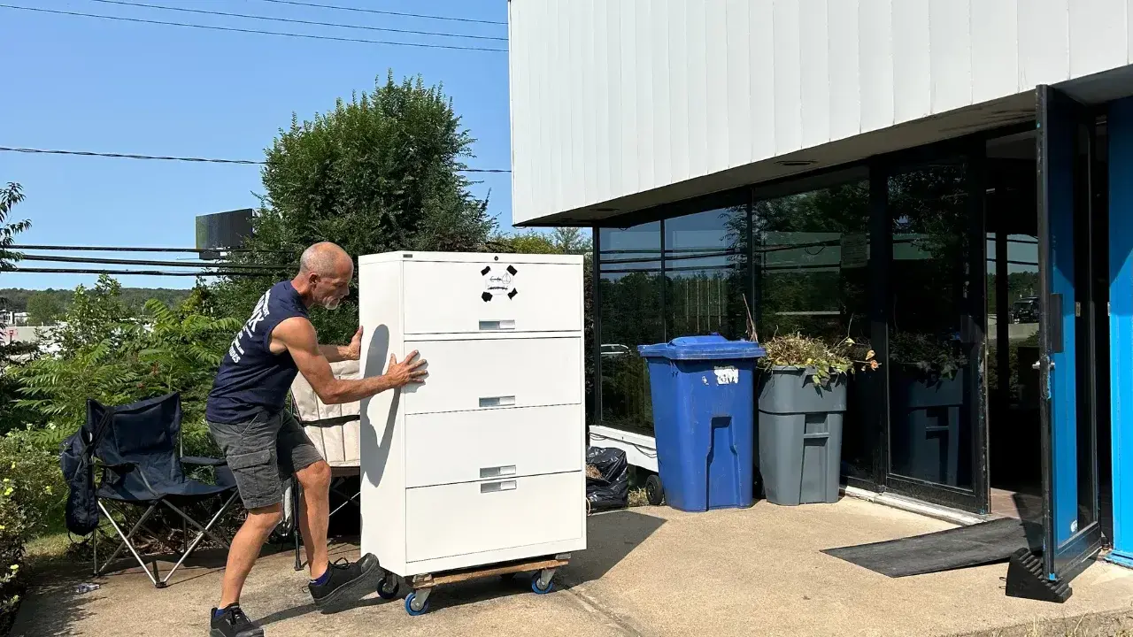 Déménageur déplaçant un classeur de bureau sur roulettes devant un bâtiment commercial Déménageur déplaçant un classeur de bureau sur roulettes devant un bâtiment commercial