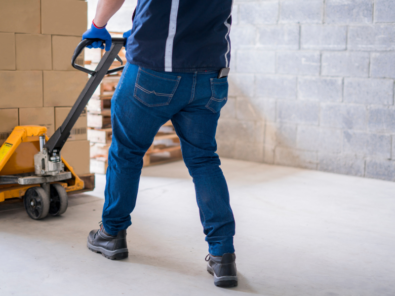 Person using a pallet jack to move a pallet of boxes in a warehouse.