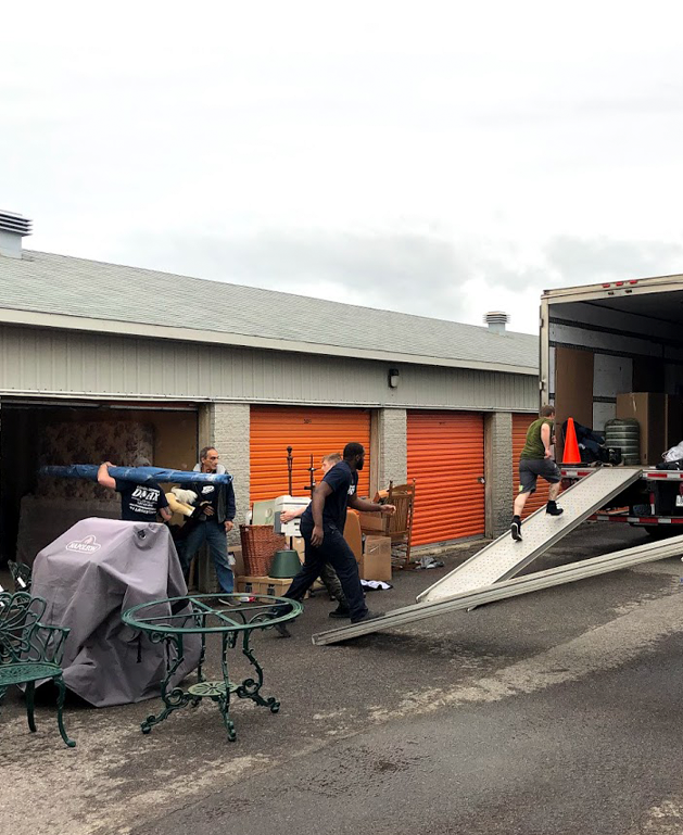 Déménageurs vidant un espace d'entreposage avec des meubles et des boîtes, chargeant un camion à l'aide de rampes.