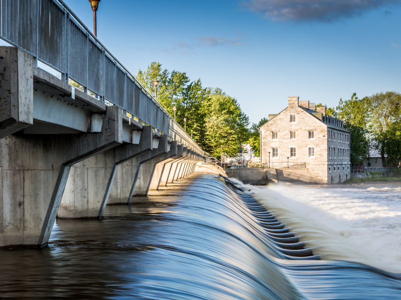 déménagement Terrebonne : Vue du barrage et du vieux moulin de Terrebonne au Québec, avec de l'eau en cascade sous un pont en béton, et un bâtiment historique en pierre en arrière-plan