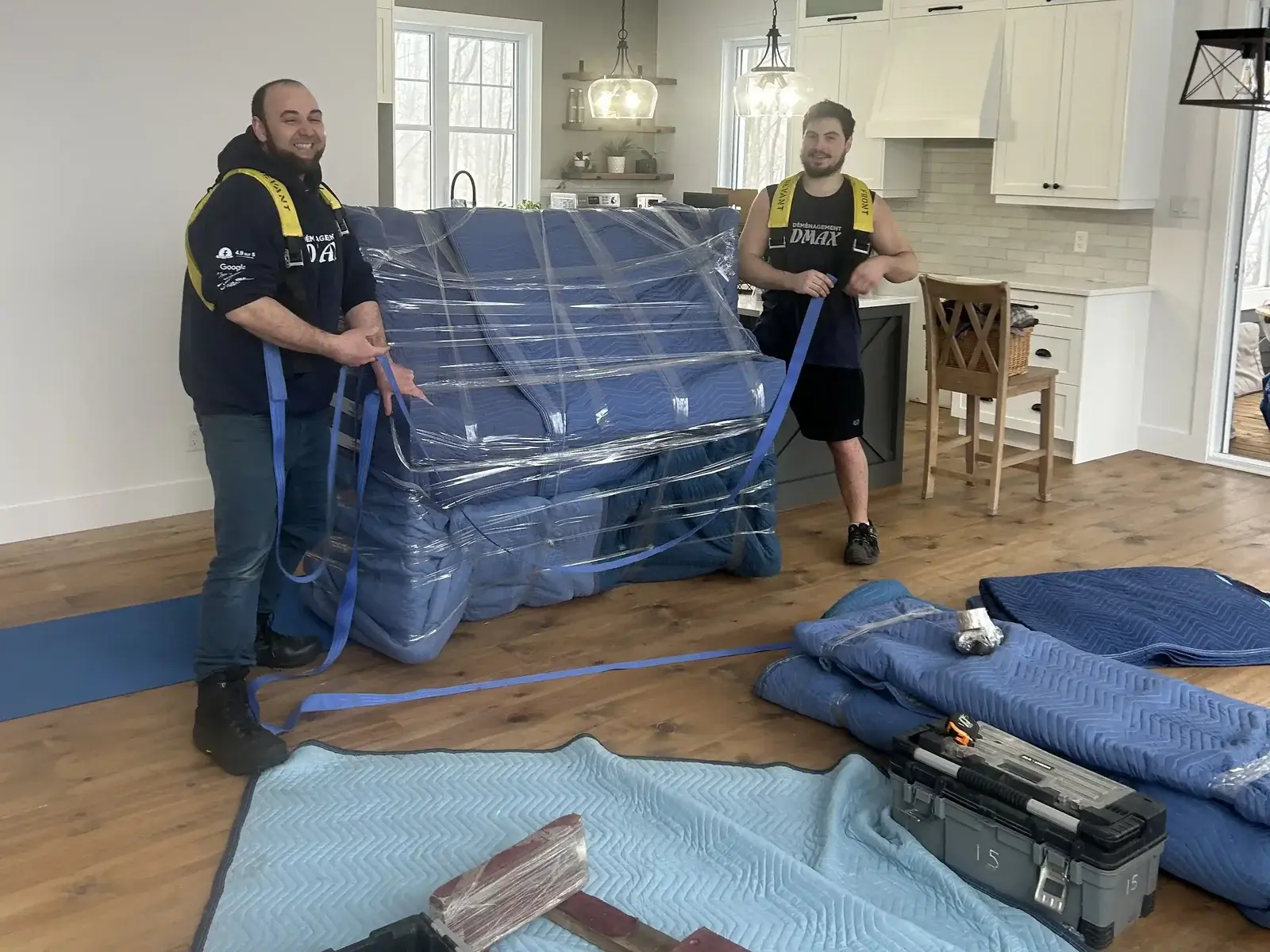 Moving Terrebonne: two Déménagement DMAX movers wrap a piece of furniture in padded blankets and plastic film